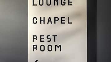 Ein Hinweisschild mit dem Text 'BUSINESS LOUNGE CHAPEL REST ROOM' und einem nach links zeigenden Pfeil.