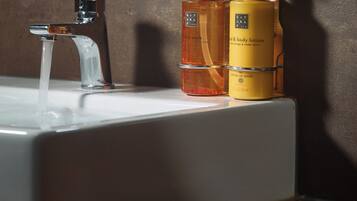 A bathroom sink with running water, two bottles of hand wash and body lotion, and a wooden countertop.