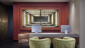 En receptionsdisk med två Apple iMac-datorer, ett träskåp märkt med texten ”THE ICON” och två gröna fåtöljer.
