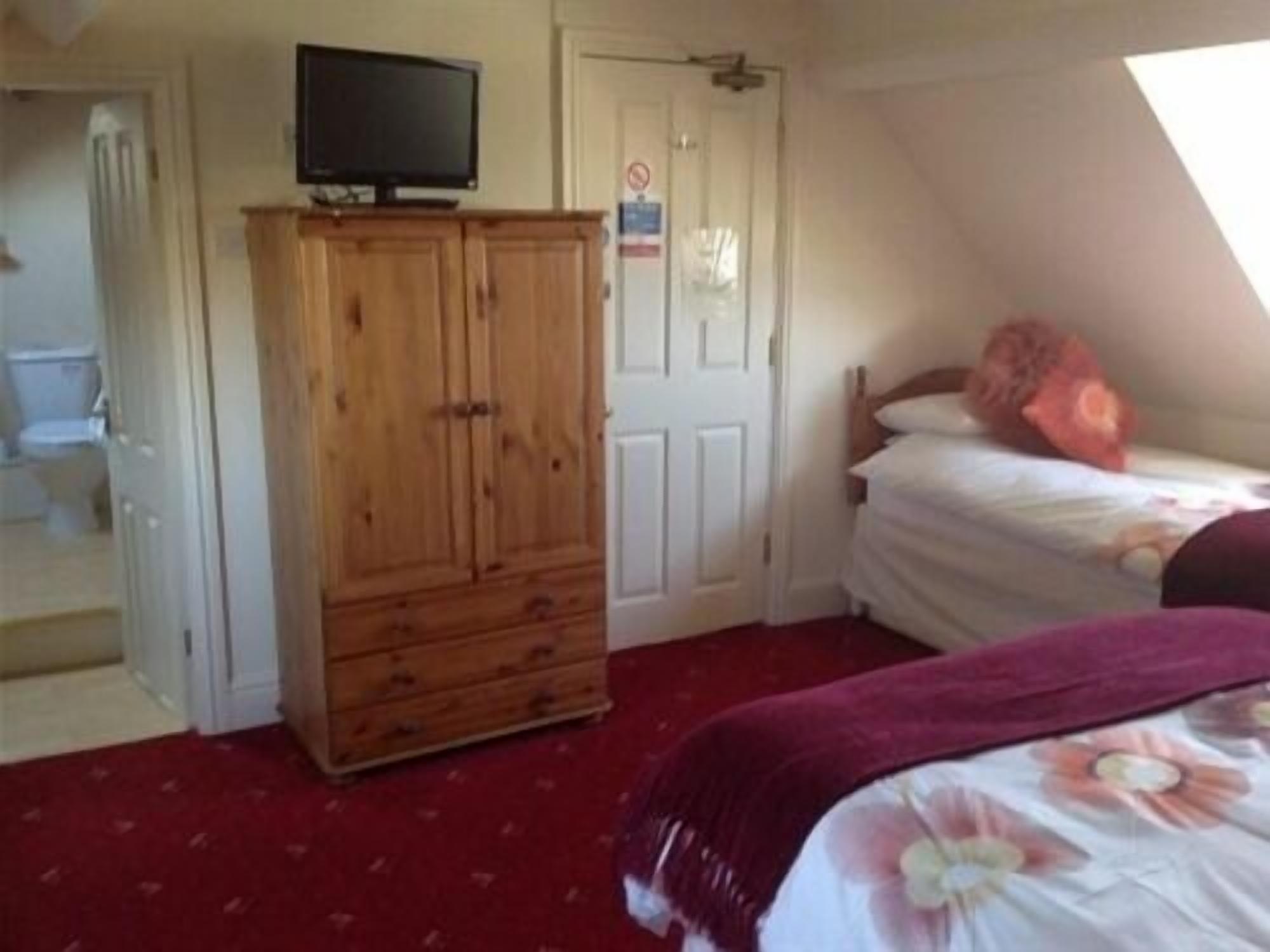 Un dormitorio con un armario de madera, una cama con colcha floral y un televisor encima del armario.