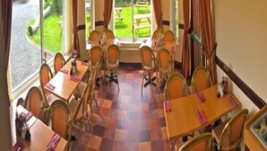 Een eetgedeelte met geruit vloerkleed, rieten stoelen en tafels gedekt voor vier personen.