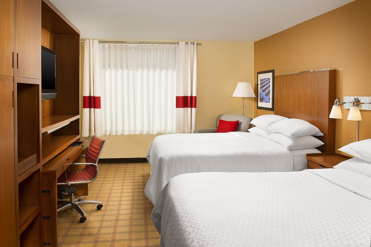 Habitación de hotel con dos camas, un escritorio, una silla, un televisor y una ventana con cortinas.