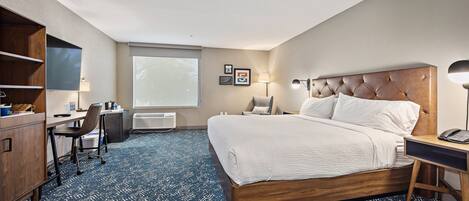 A hotel room with a large bed, a desk with a chair, a wardrobe, and a large window.