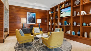Un vestíbulo moderno con pared de madera, un televisor grande, una estantería y sillones amarillos.
