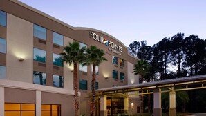 Un hotel llamado Four Points by Sheraton con una fachada moderna, ventanas amplias y un área de entrada cubierta.