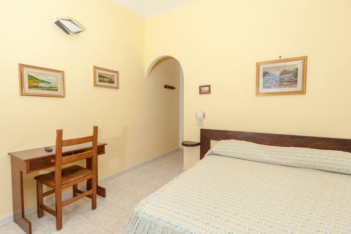 Een kamer met een bed, een bureau en twee foto's in lijsten aan de muur.