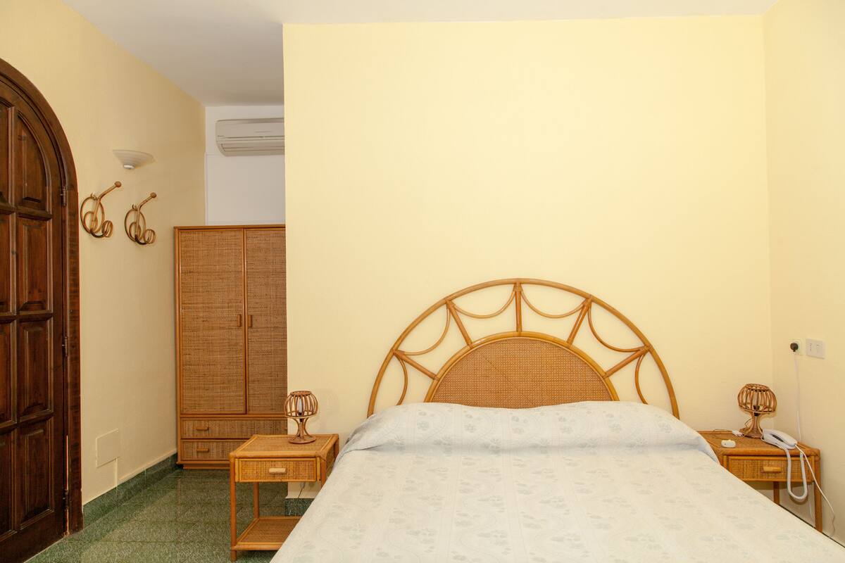 Een slaapkamer met een bed, een houten garderobe, nachtkastjes en een wandairconditioning.