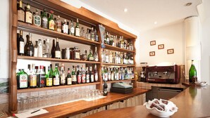 Uma área de bar com prateleiras cheias de garrafas de bebidas, copos e uma máquina de café.
