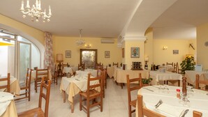 Uma área de refeições com várias mesas e cadeiras, um candelabro e vista para o exterior.
