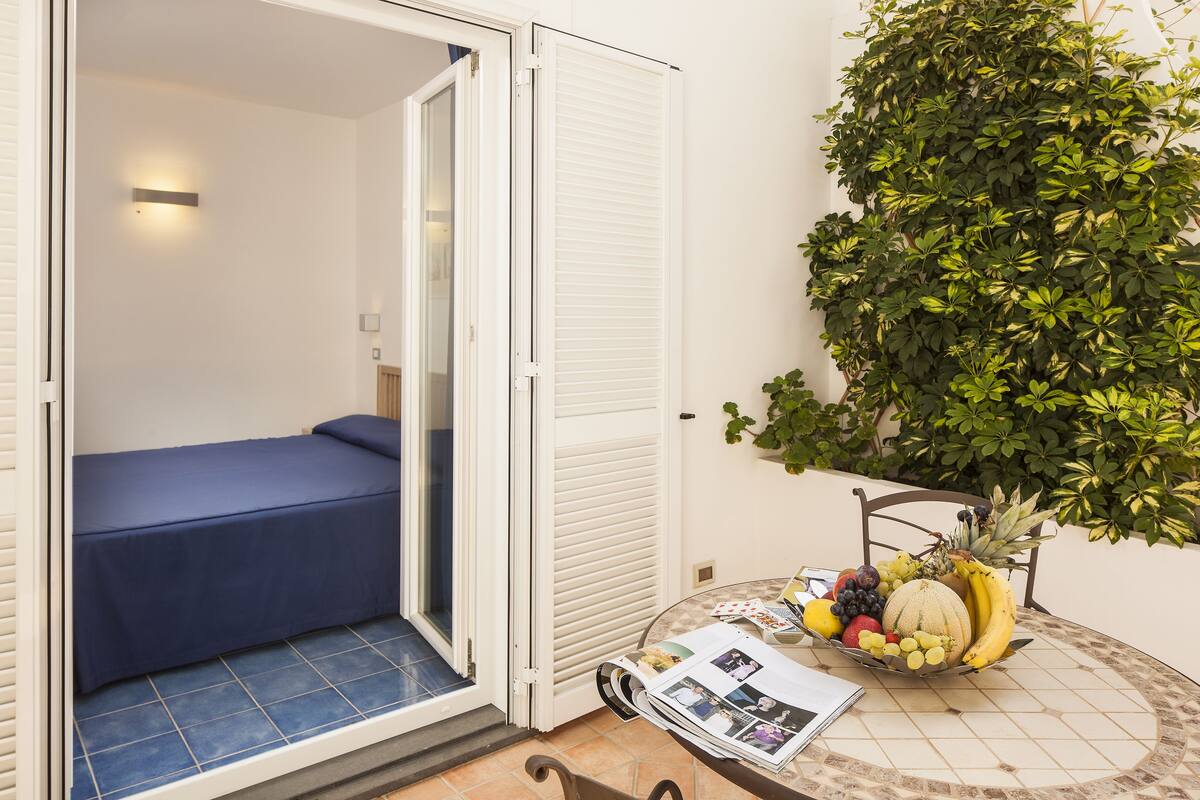 A small room with a bed, a table with a fruit bowl, and a potted plant.