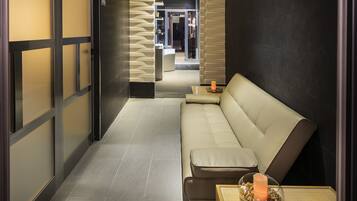 Une salle de spa moderne avec un canapé beige, une petite table sur laquelle est posée une bougie, et une vue sur l’espace de soins.