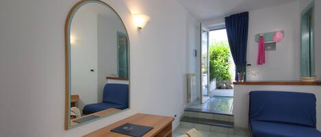 Una habitación con un escritorio de madera, una silla, un sofá azul, un espejo grande y vistas al exterior.
