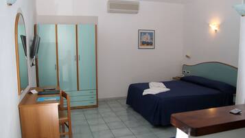 Habitación de hotel con cama, escritorio con silla, armario, espejo y televisor montado en la pared.