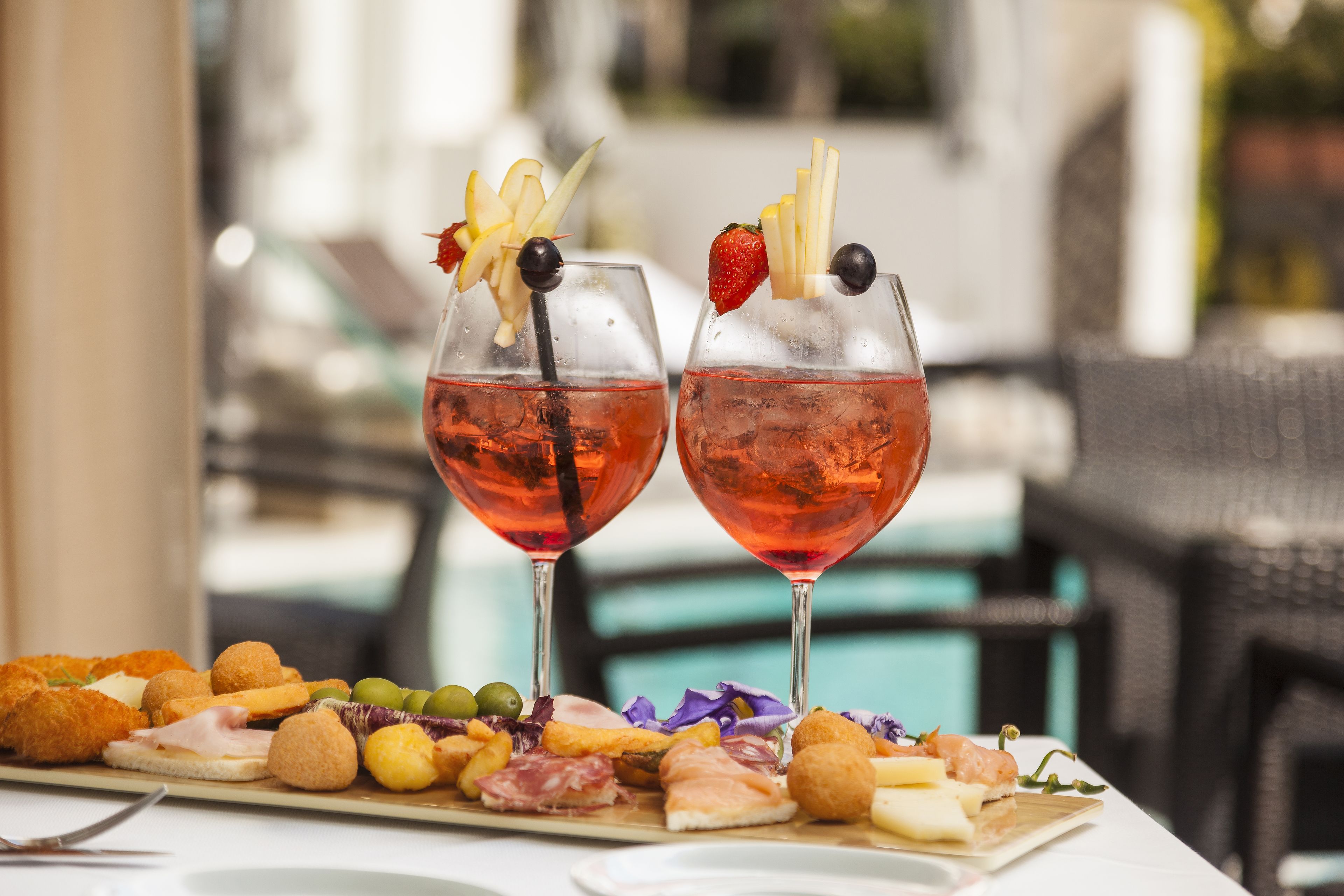 A table with a charcuterie board and two glasses of red wine with garnishes.