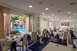 A dining area with tables set for breakfast, overlooking a pool and greenery. - Grifo Hotel Charme & SPA (Casamicciola Terme)
