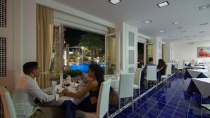 Un restaurante con vista a una piscina, sillas blancas y piso de azulejos azules.