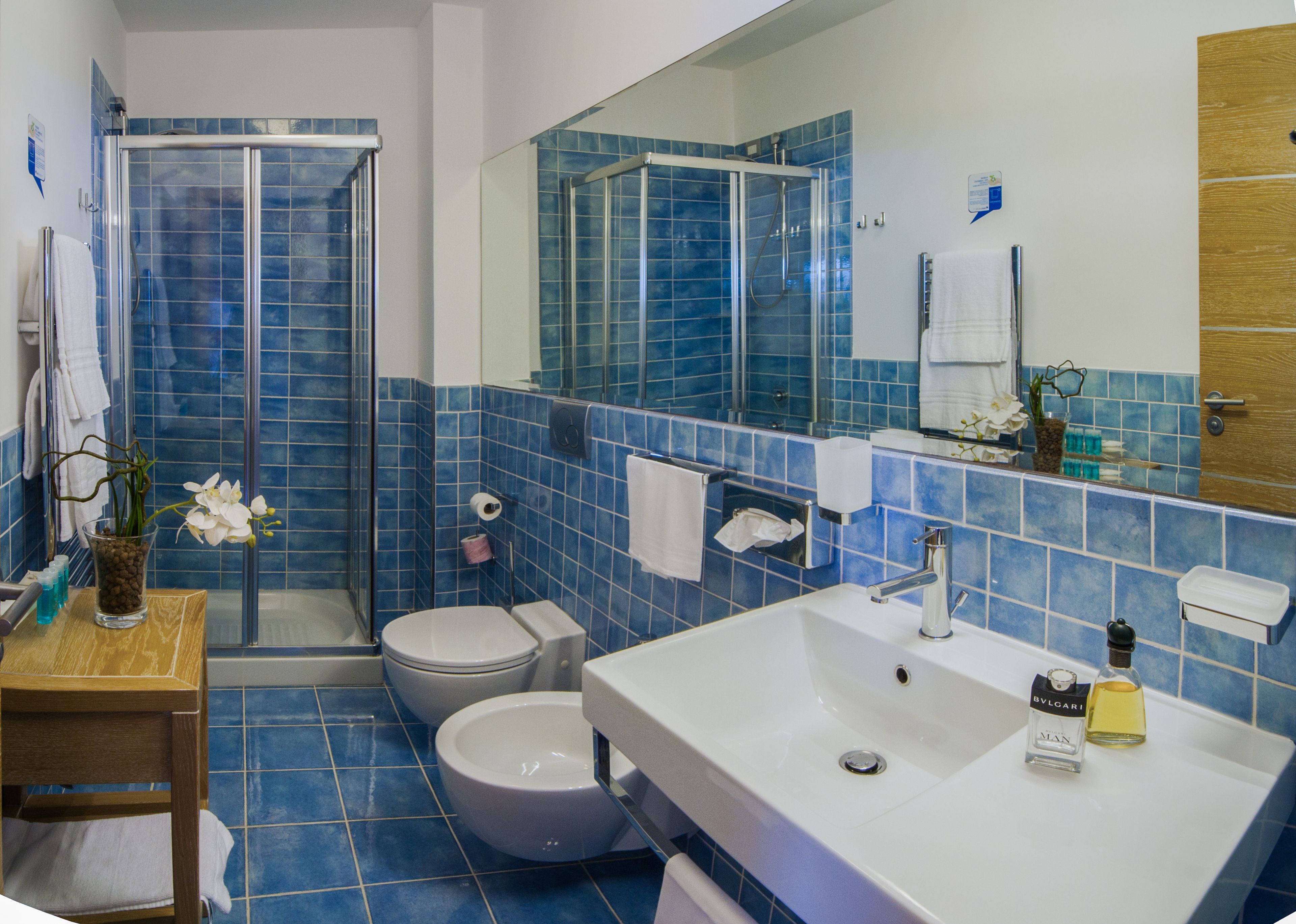 A bathroom with blue tiles, a shower, a toilet, a sink, and a mirror.