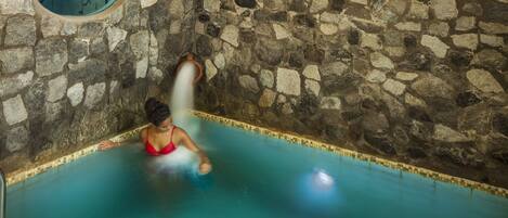 Una piscina interior con paredes de piedra y borde de azulejos.