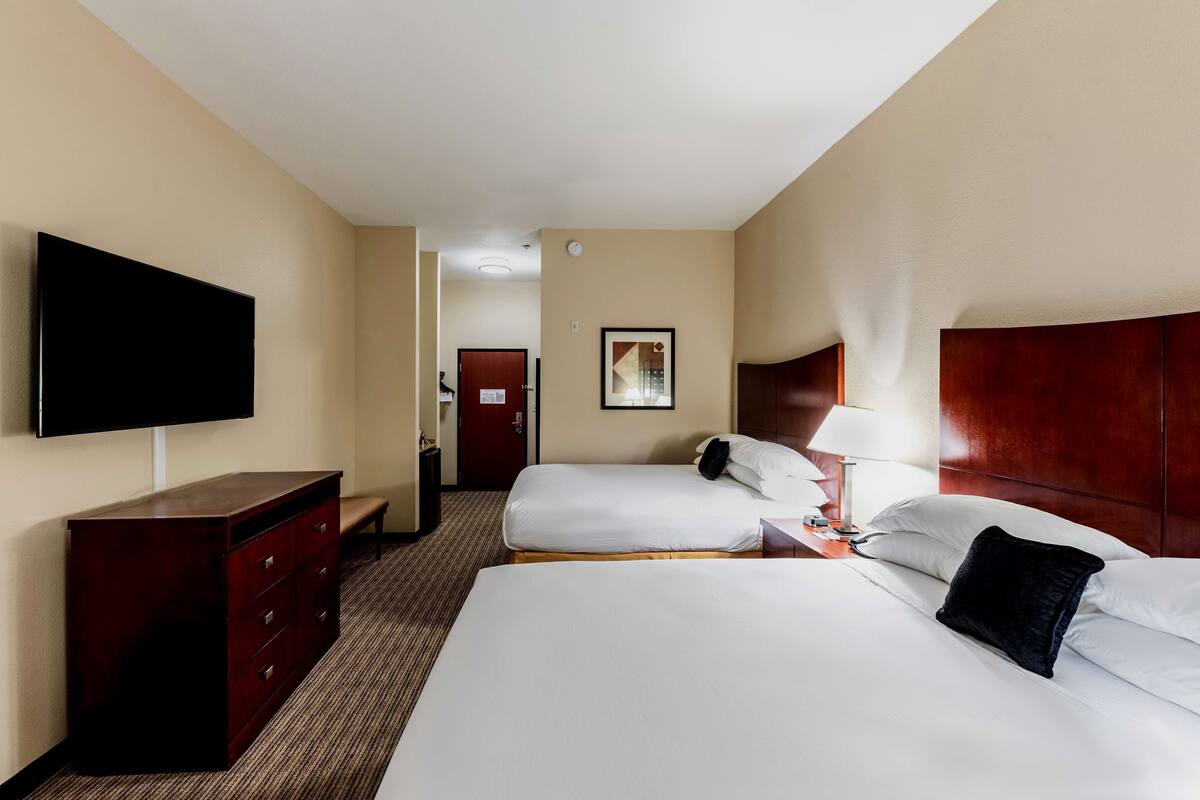 A hotel room with a large bed, a dresser, a television, a bedside table with a lamp, and a framed picture on the wall.