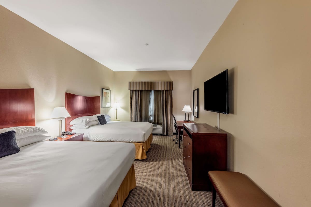 A hotel room with two beds, a desk, a TV, and a bench.