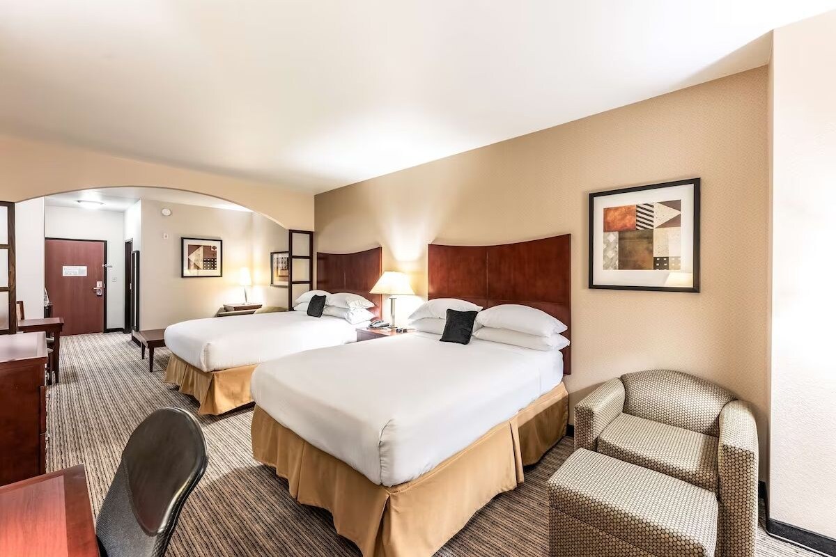 A hotel room with two beds, a desk, a chair, and a framed picture on the wall.