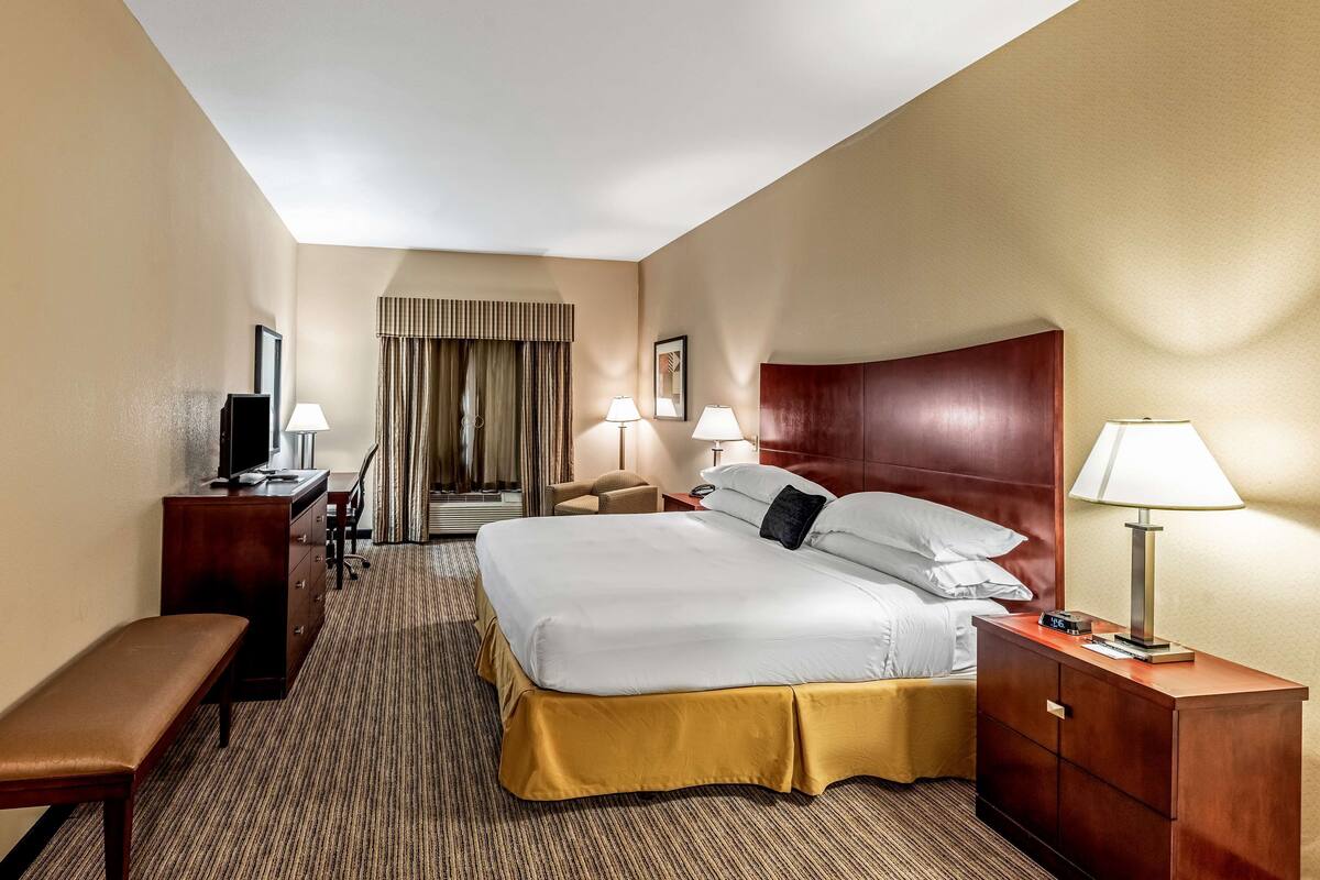 A hotel room with a large bed, a desk, a chair, a bench, and a television.