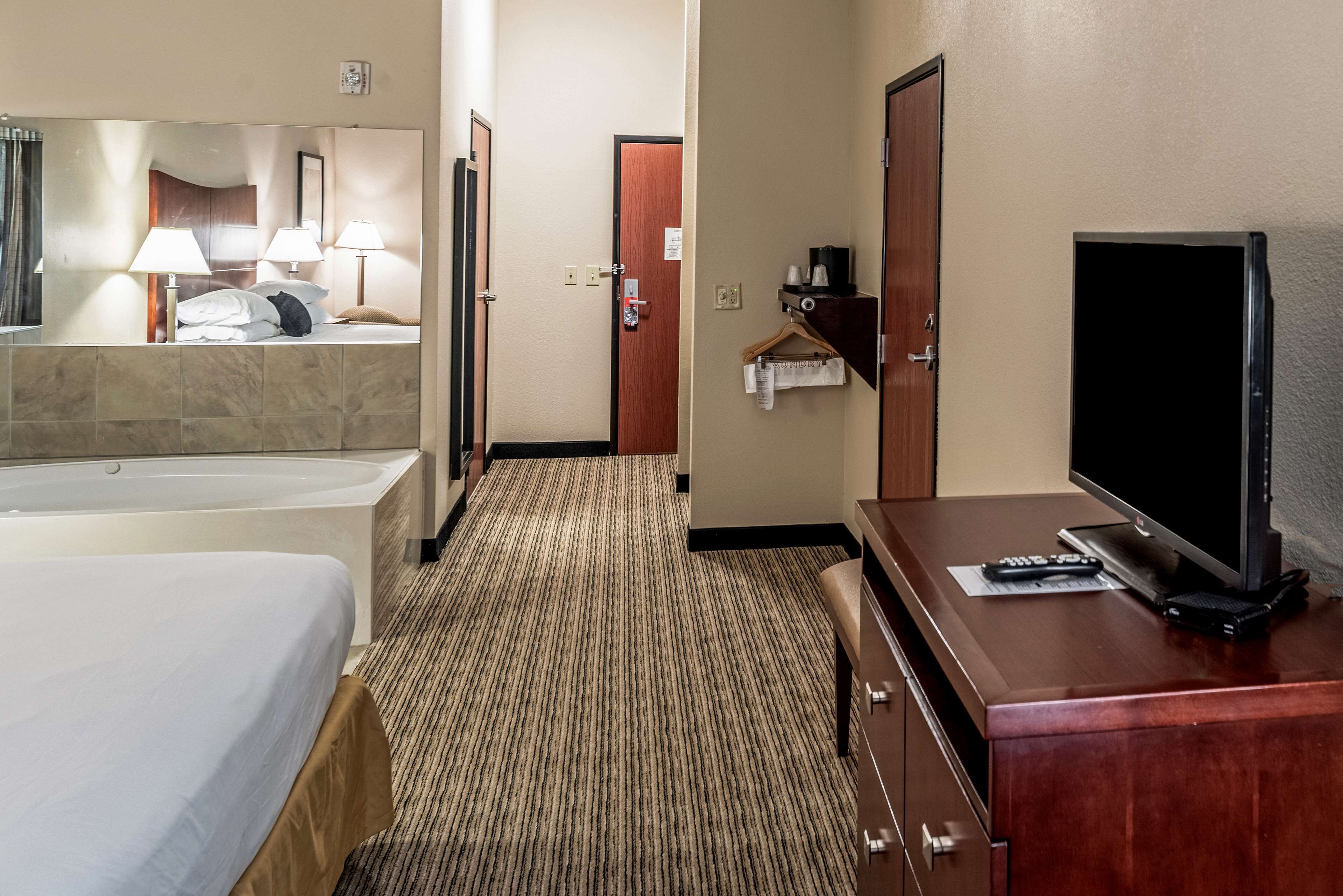 A hotel room with a bed, a large mirror, a TV, a desk, and a bathroom with a bathtub.