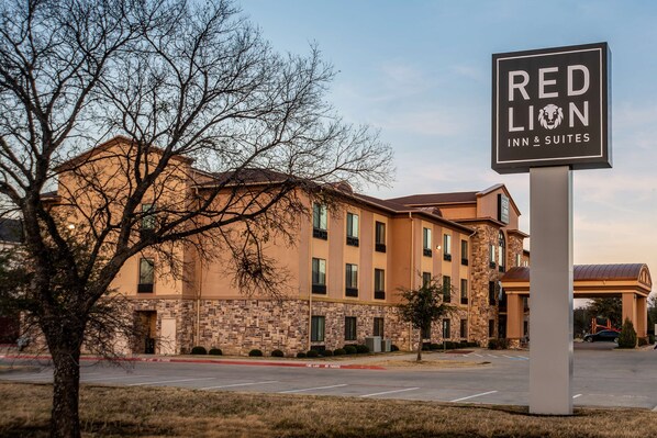 A Red Lion Inn & Suites building with a stone facade, multiple windows, and a parking lot in front. - Red Lion Inn & Suites Mineral Wells (Mineral Wells)