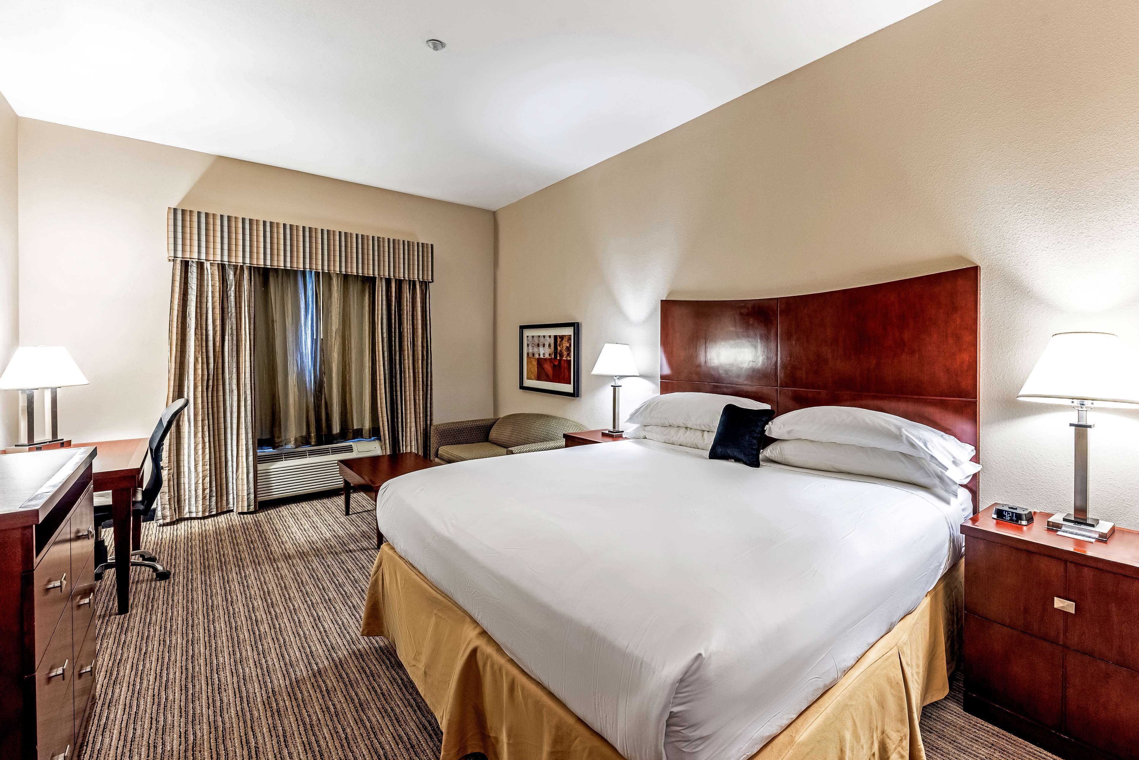 A hotel room with a large bed, a desk, a chair, a lamp, and a picture on the wall.