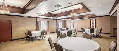 Een congreszaal met ronde tafels en stoelen, houten lambrisering en inbouwverlichting.