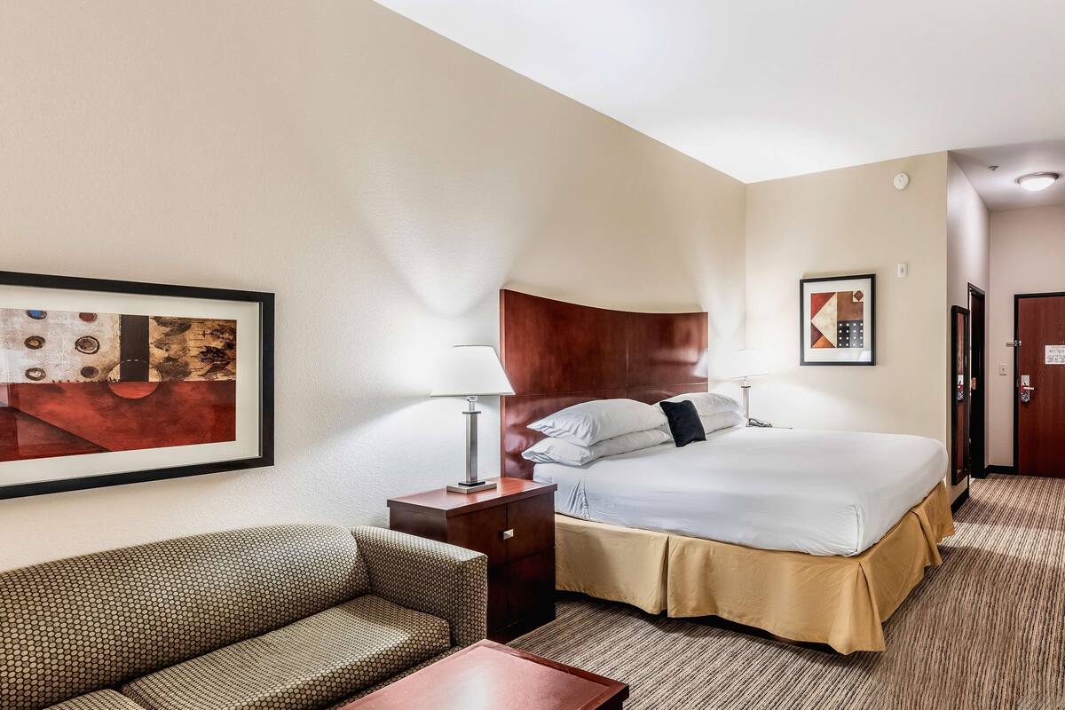 A hotel room with a bed, a sofa, a nightstand, and two framed pictures on the wall.