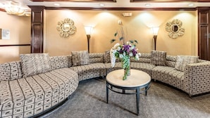 A modern lounge area with a patterned sofa set, a round coffee table, and decorative wall sconces. - Red Lion Inn & Suites Mineral Wells (Mineral Wells)