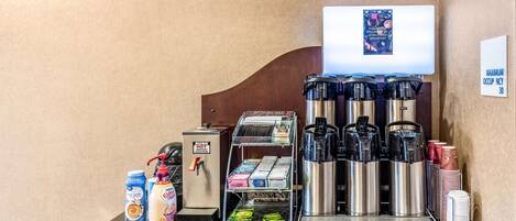 En kaffestation med en varmvattenbehållare från DUNKIN', kaffebryggare och ett stort utbud av kaffekapslar.