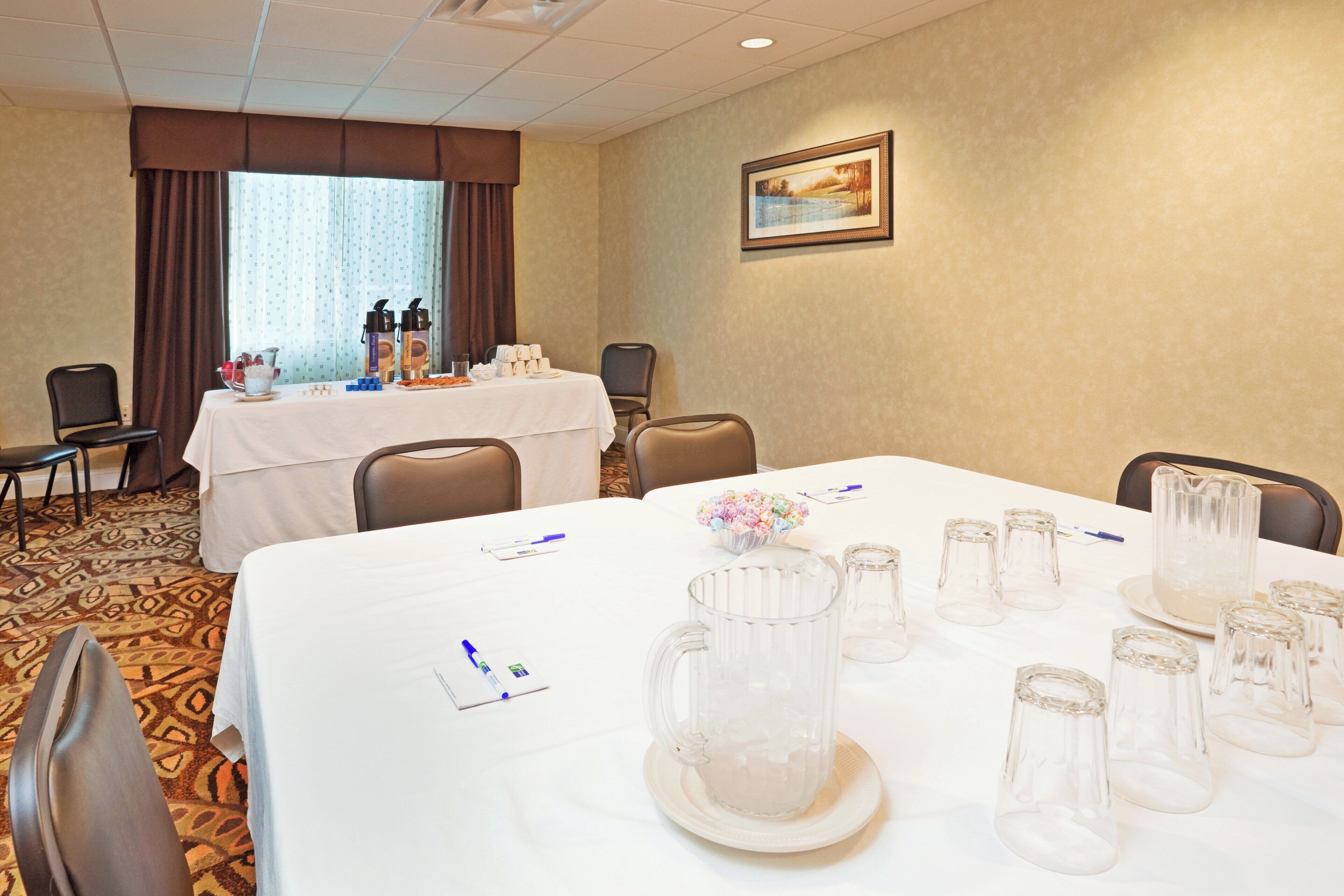 A conference room with a white table set for a meeting, equipped with glassware, pens, and a floral centerpiece.