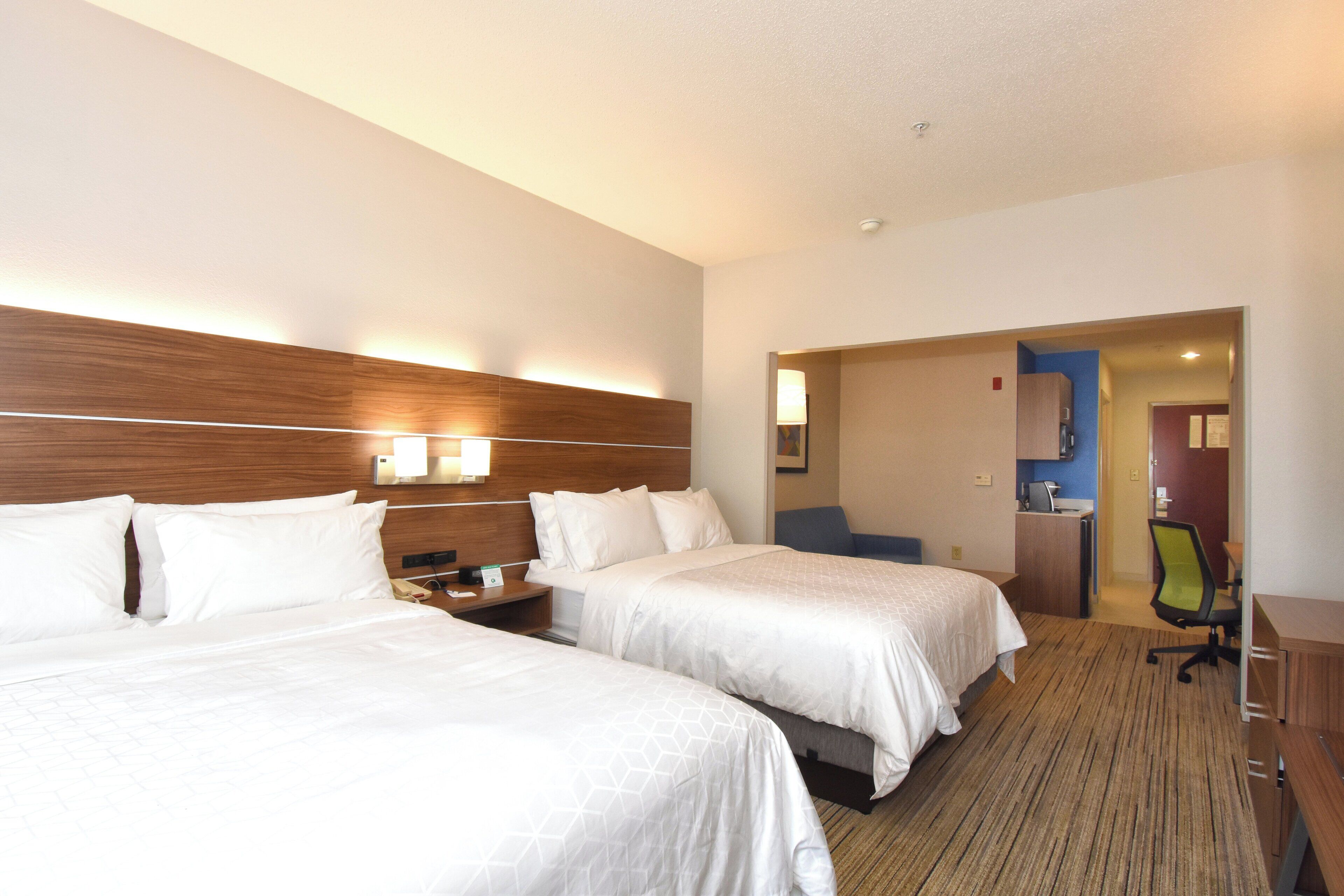 A hotel room with two beds, a desk, a chair, and a small kitchenette.