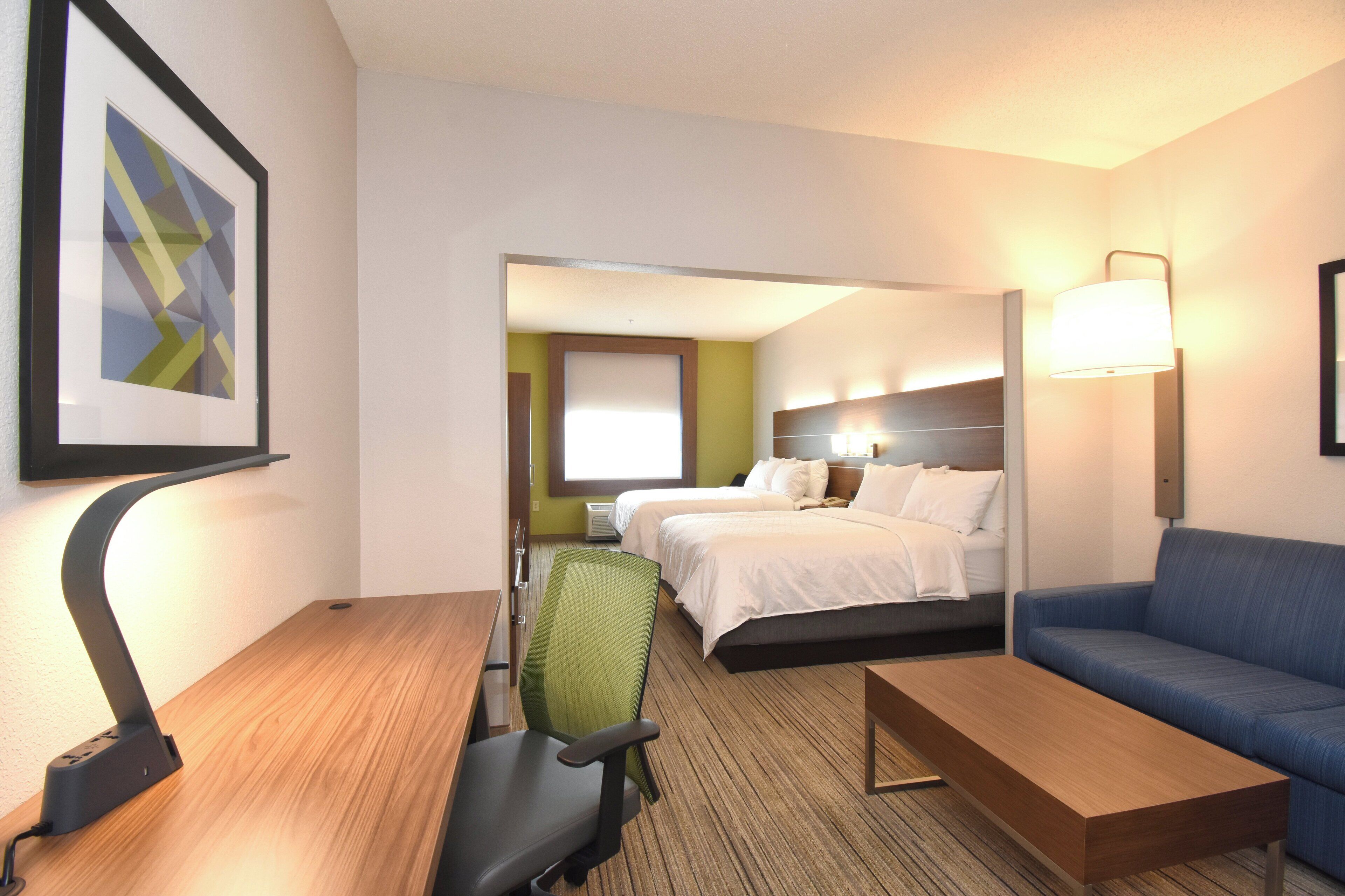 A hotel room with a bed, a desk, a chair, a sofa, and a lamp.