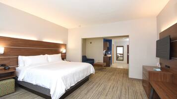 A hotel room with a large bed, bedside tables, a desk, a chair, a television, and a bathroom visible through an open door.