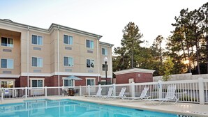 A hotel with a swimming pool, outdoor seating, and a brick building.