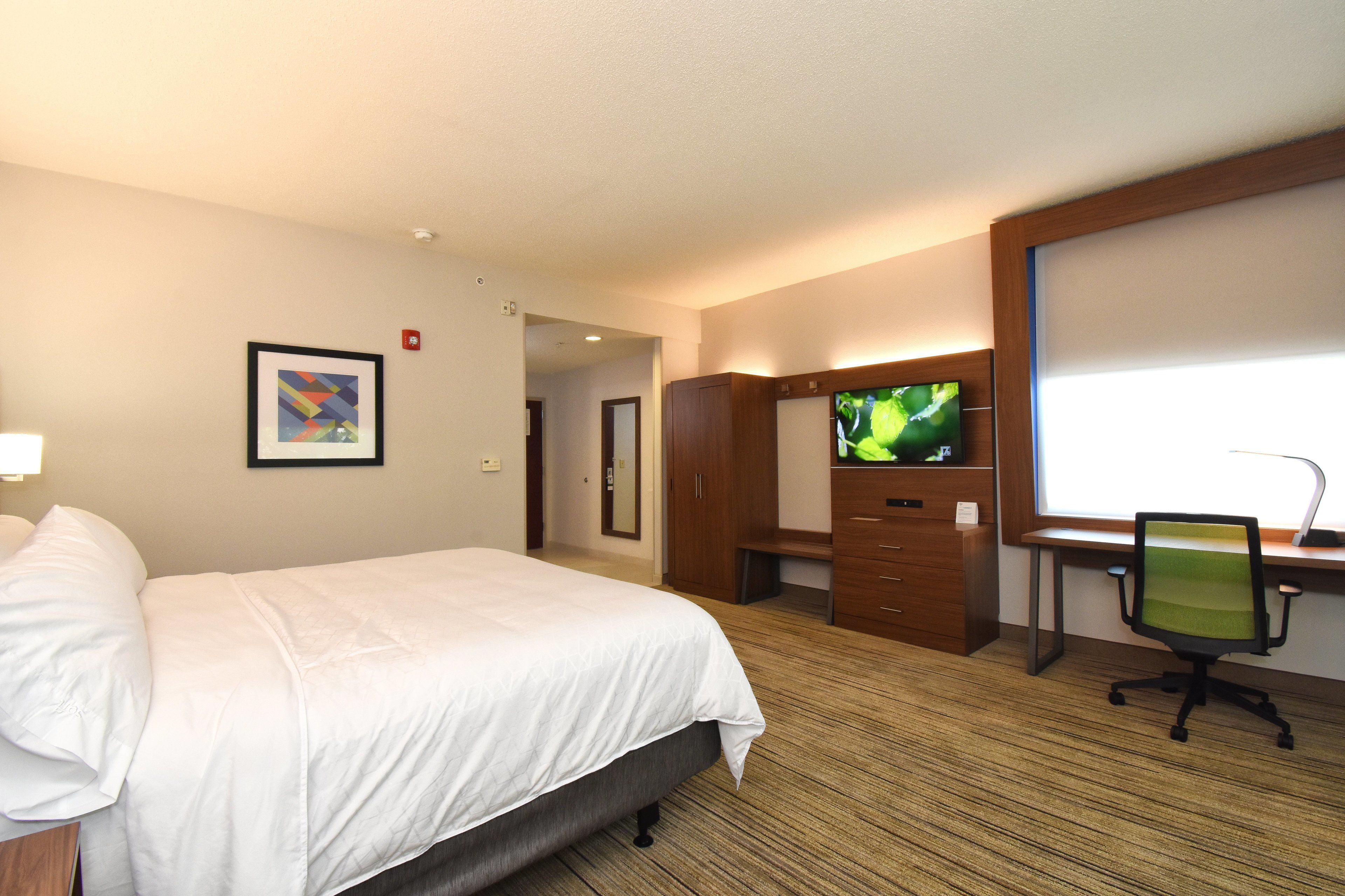 A hotel room with a bed, a desk with a computer, a television, and a framed picture on the wall.