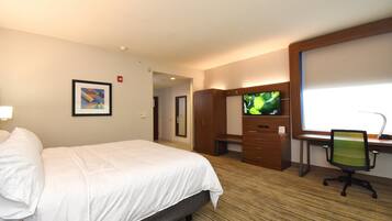 A hotel room with a bed, a desk with a computer, a television, and a framed picture on the wall.