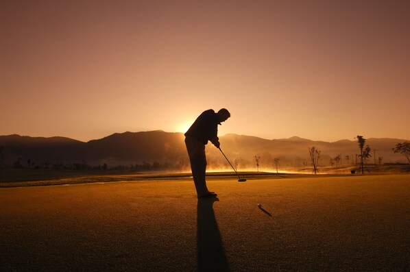 A silhouette of a person playing golf at sunset with mountains in the background. - Holiday Inn Express Hotel & Suites Southern Pines by IHG (Southern Pines)