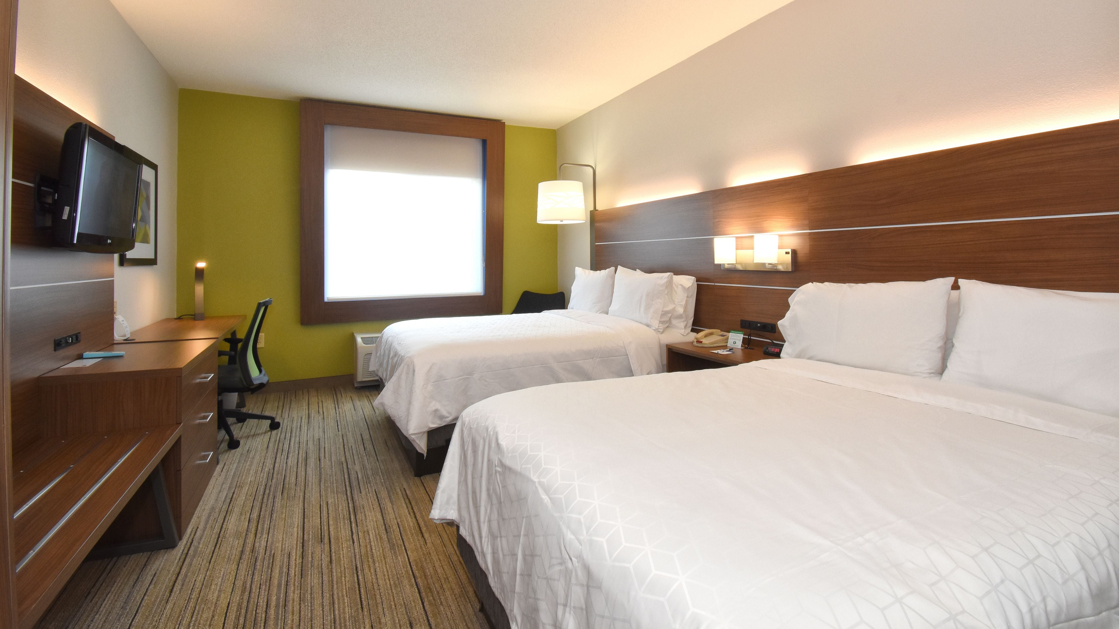 A hotel room with two beds, a desk, a chair, a TV, and a window.
