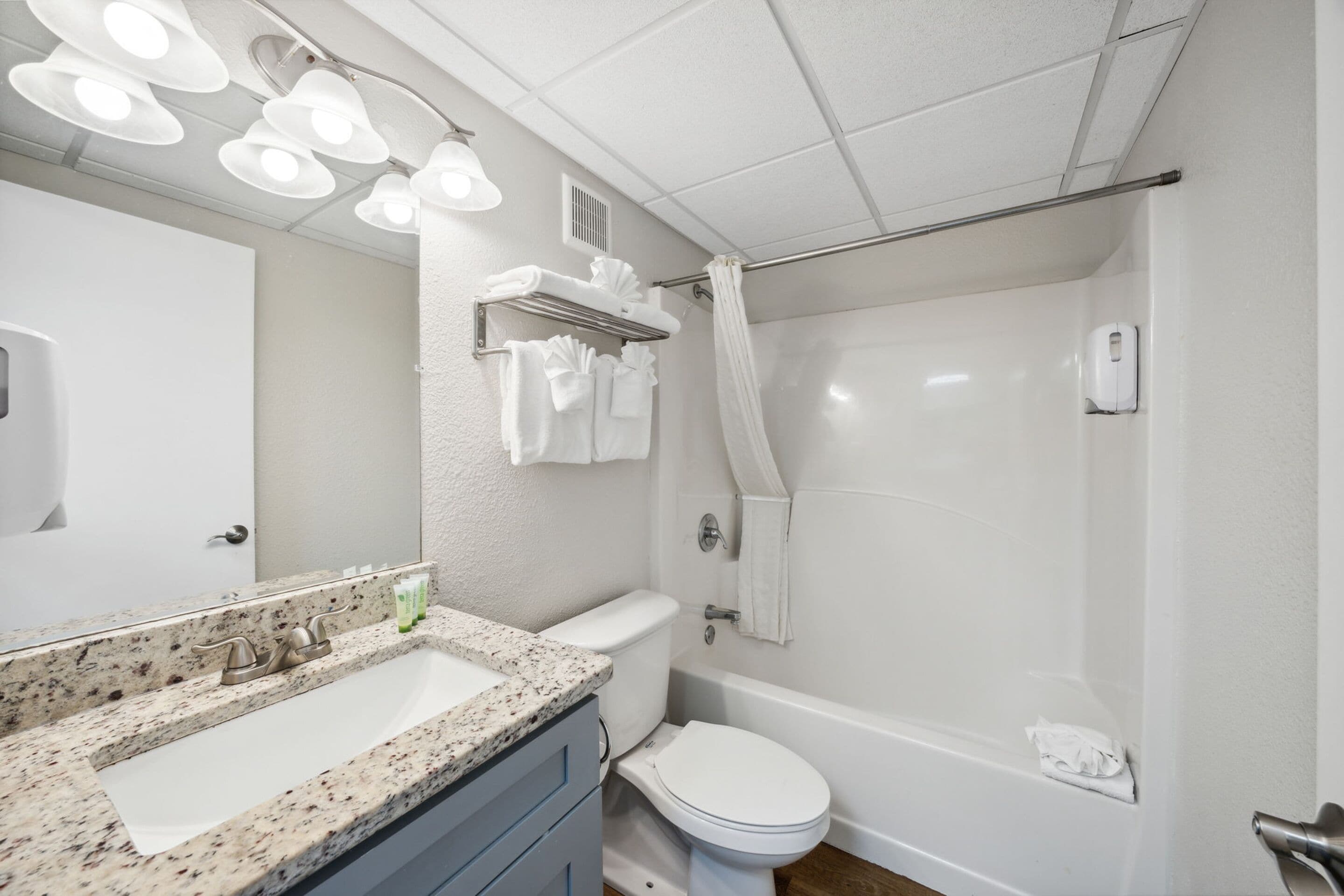 A bathroom with a granite countertop sink, a toilet, a bathtub, and a shower curtain.
