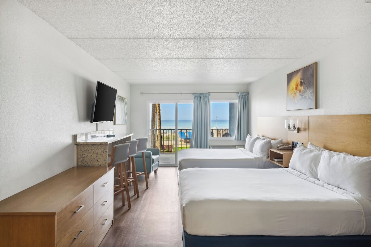 Habitación de hotel con cama, escritorio, televisión y balcón con vistas al mar.