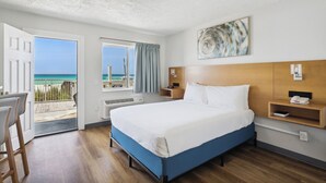 A hotel room with a bed, a desk, a chair, a window with a view of the beach, and a ceiling light.