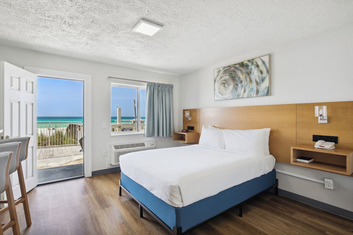 Habitación de hotel con cama, escritorio, silla, ventana y vista a la playa, además de una lámpara de techo.