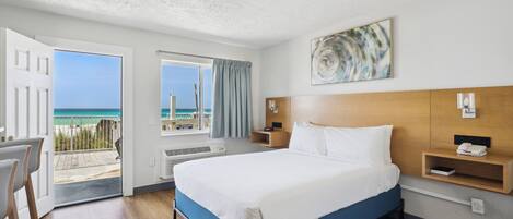 Une chambre d’hôtel comprenant un lit, un bureau, une chaise, une fenêtre donnant sur la plage et un luminaire au plafond.