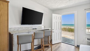 A kitchen with a TV, bar stools, and a door leading to a balcony with a view of the beach.