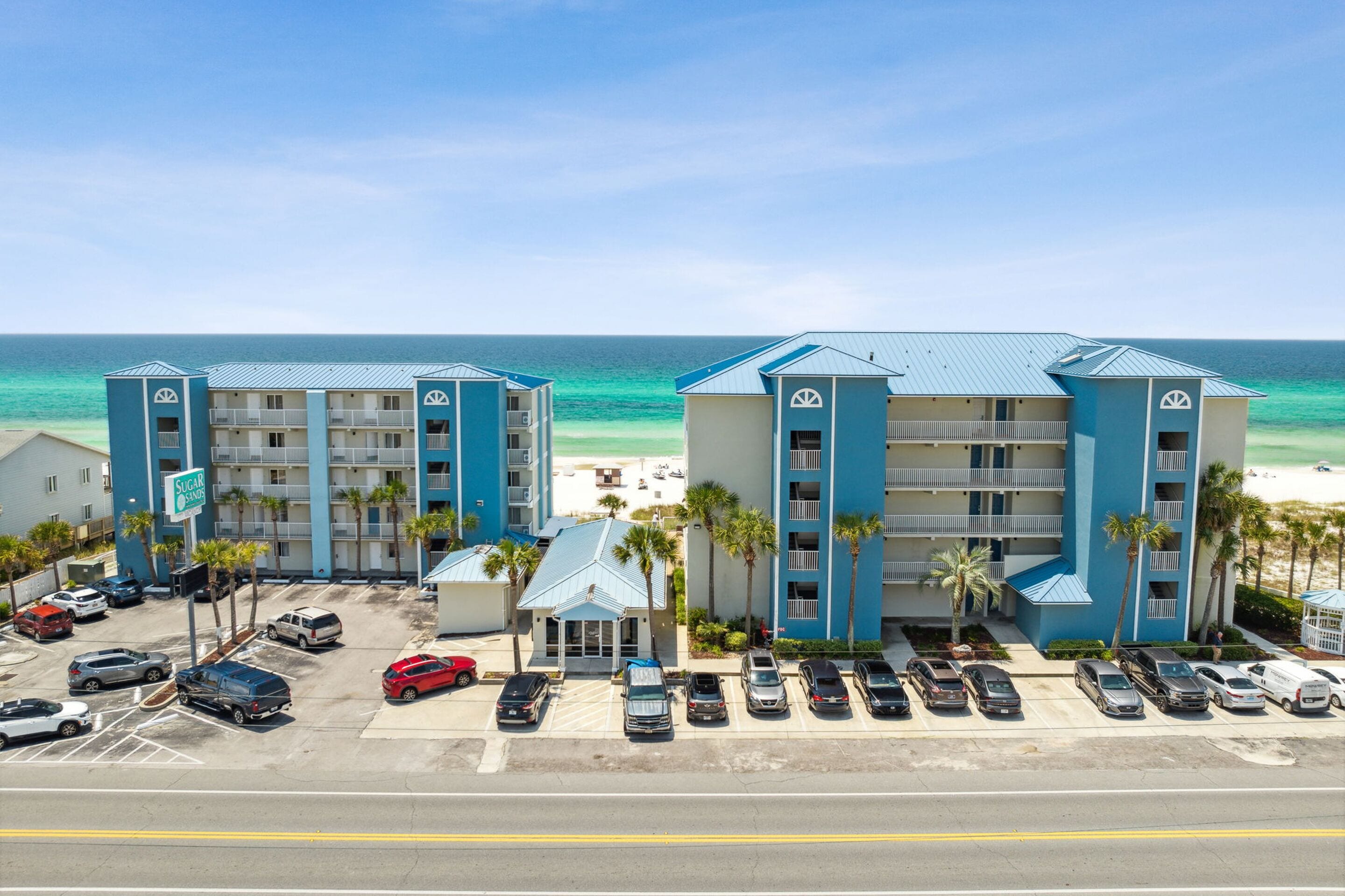 A beachfront hotel with multiple floors, a parking lot, and a view of the ocean.