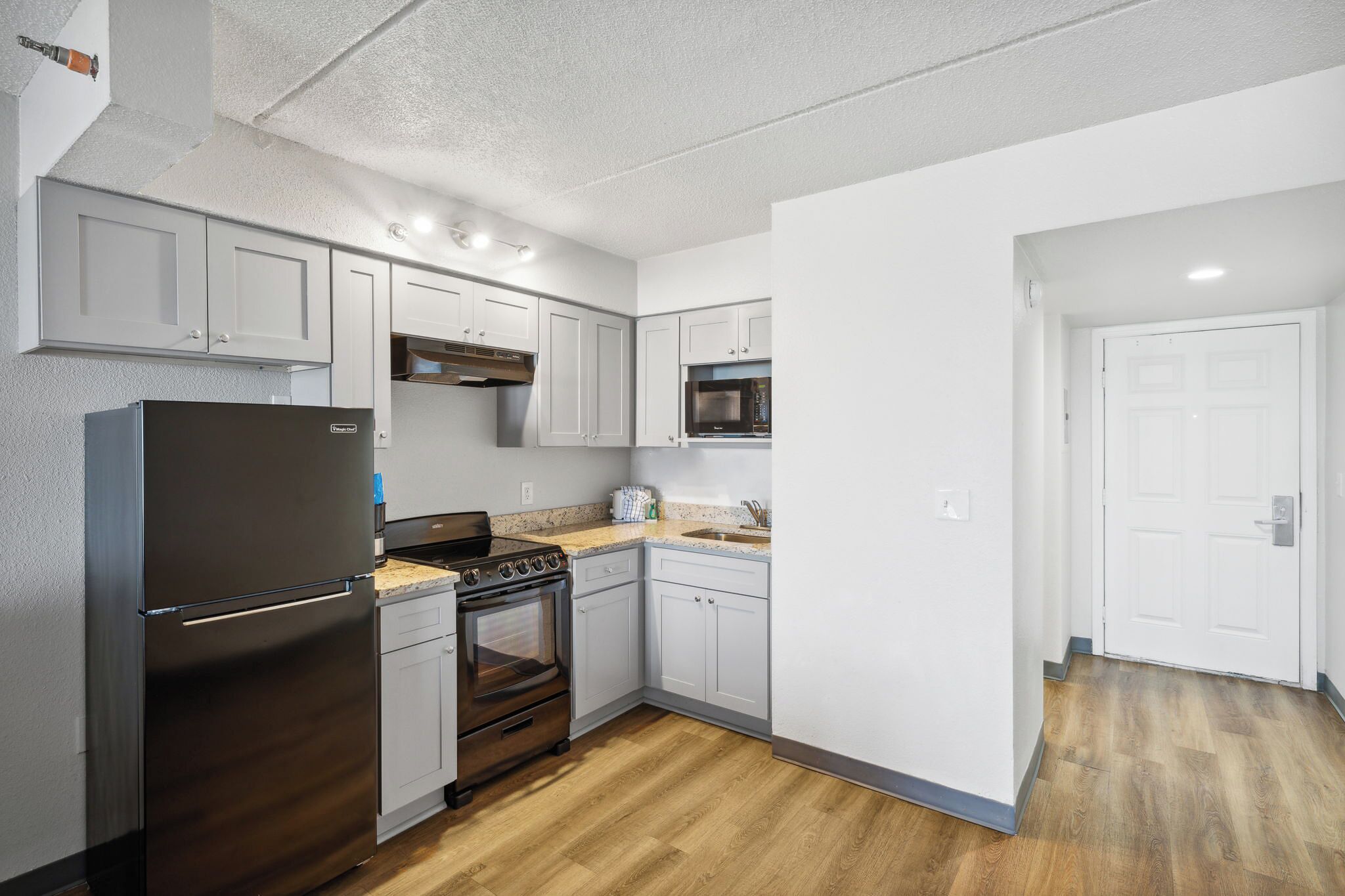 Una cocina moderna con armarios blancos, un refrigerador de acero inoxidable, un microondas y un horno empotrado.